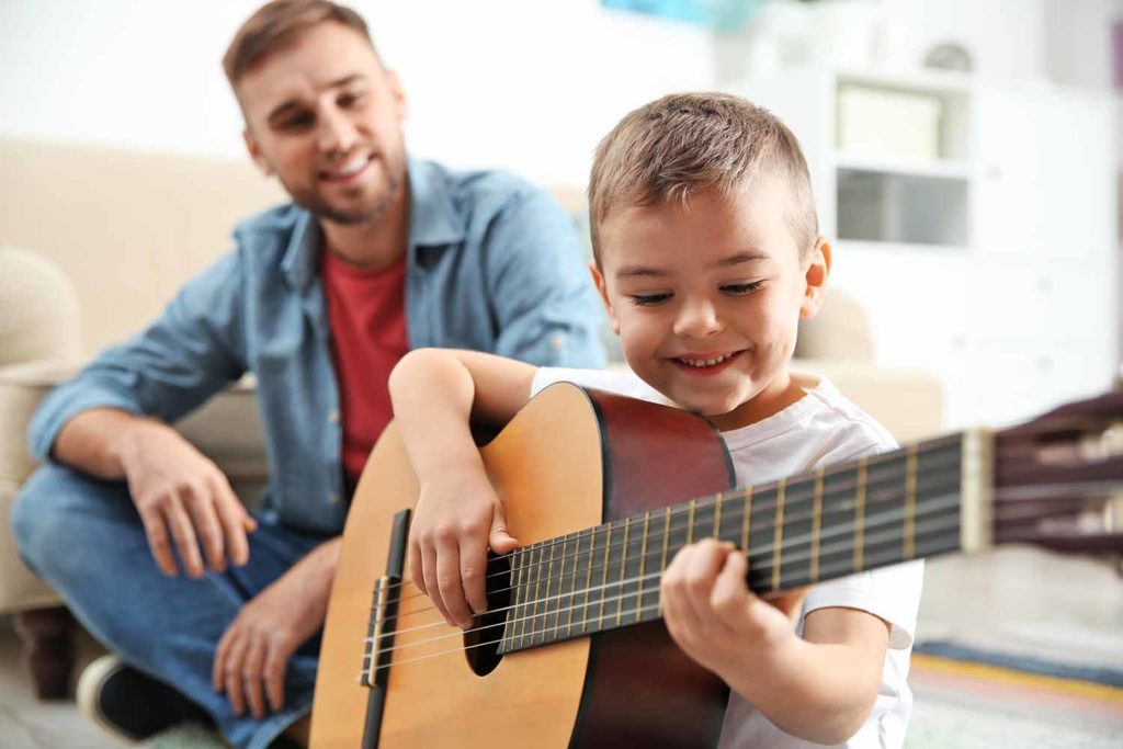 boy learning to play guitar from guitar teacher